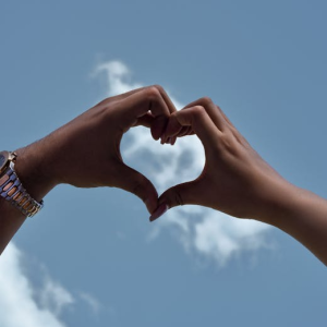 Hands forming a heart shape against a bright blue sky symbolizing love and unity.